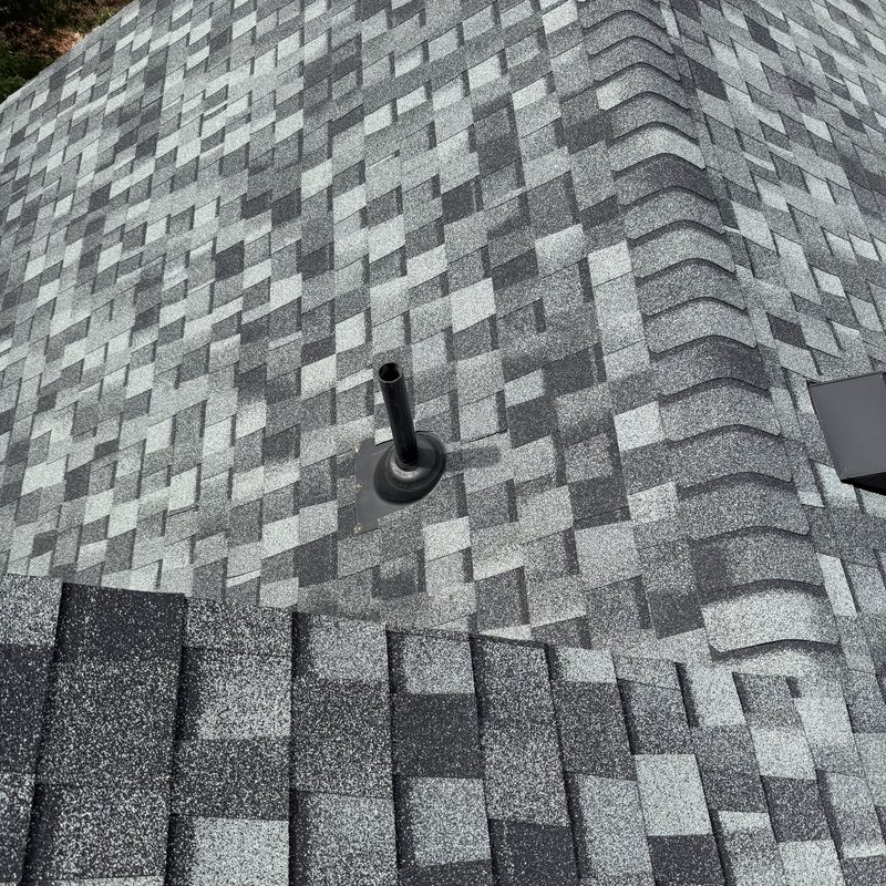 Close view of gray architectural shingles and a hip cap around a pipe vent on a finished roof