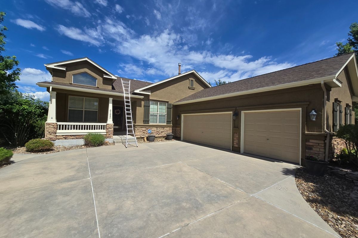 Tan ranch home with gutters and a ladder set at the roof edge