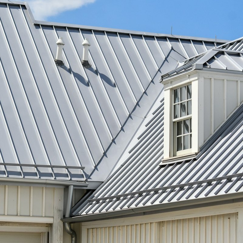 Gray standing-seam metal roof with raised seams over a dormer and a valley on a cream-sided house