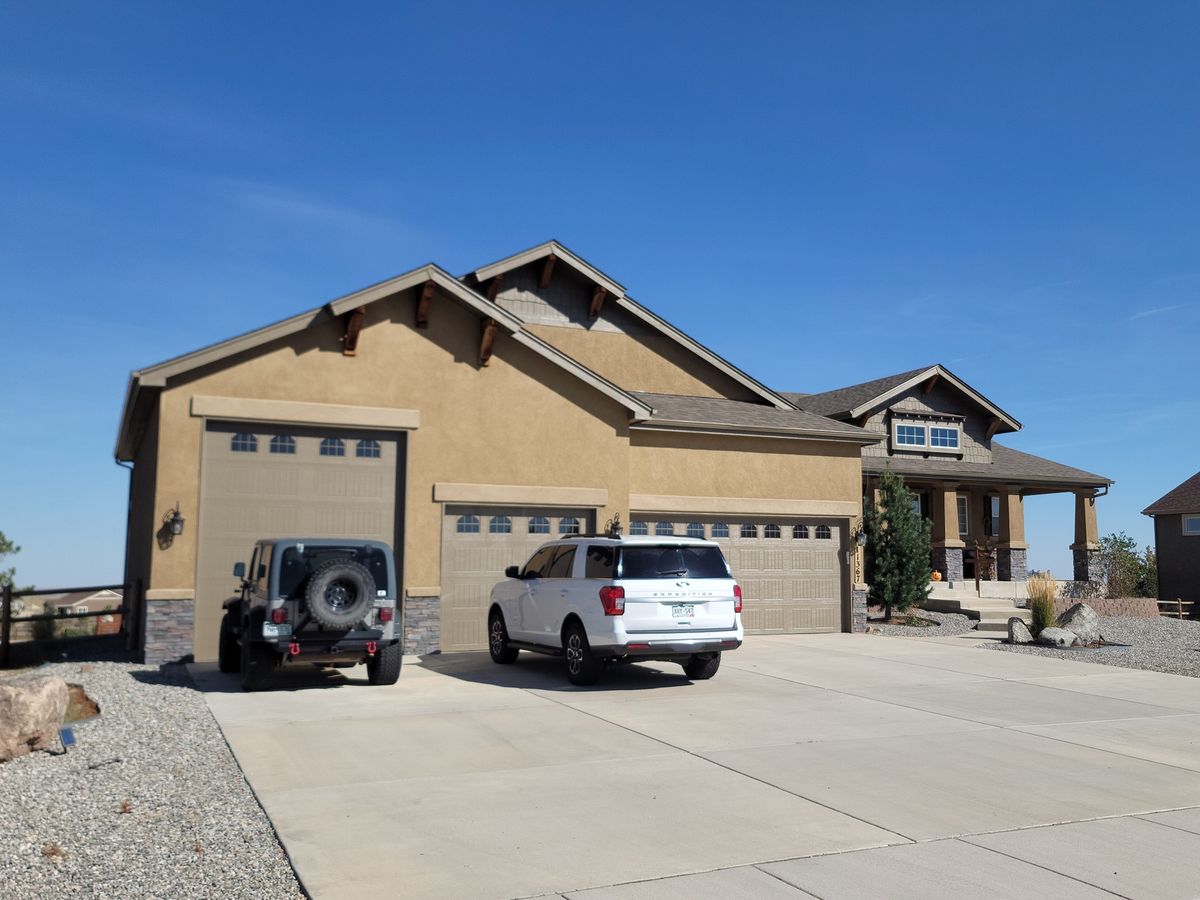Tan home with a three-car garage, finished shingle roof, and a broad concrete driveway
