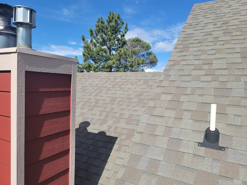 Metal vent caps on top of a chimney chase beside a finished shingle roof