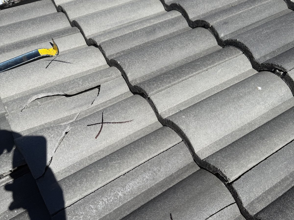 Gray tile roof with cracked pieces marked for attention beside a pry bar