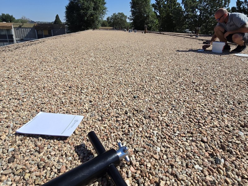 Worker completing repair work on a gravel-covered commercial roof