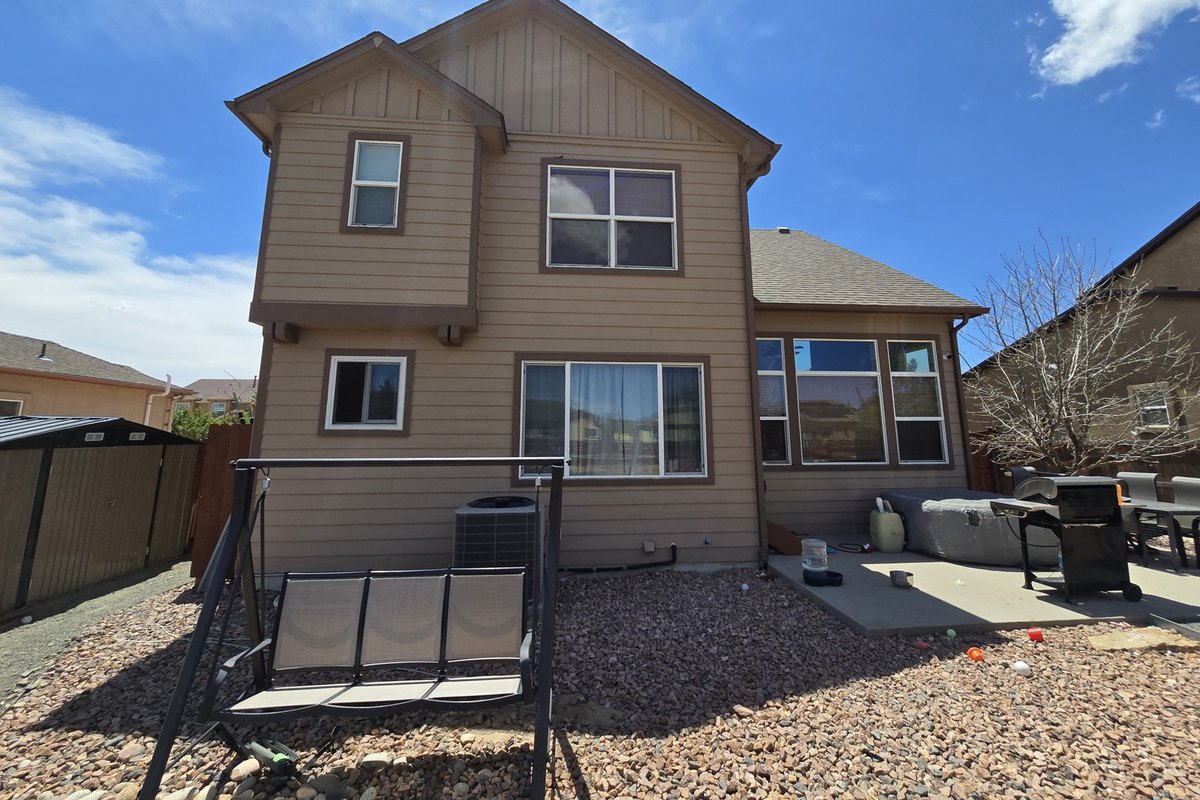 Tan two-story house with lap siding across the rear elevation and patio