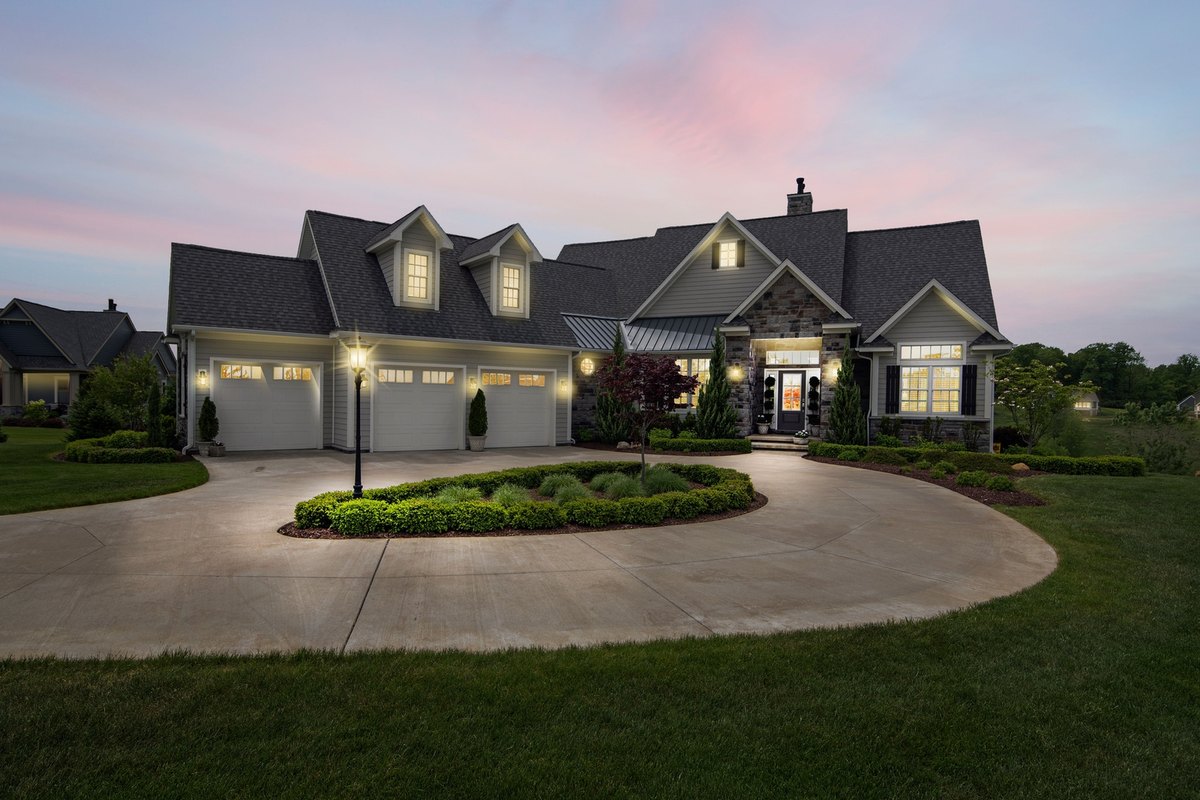 Two-story home at dusk with warm exterior lights glowing along the garages, entry, and driveway