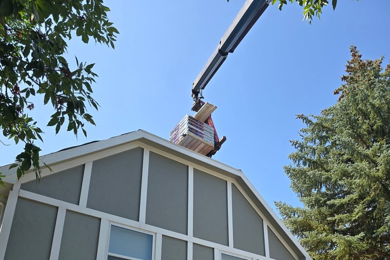 Crane lifting bundles of roofing shingles to the gable of a gambrel-roof house