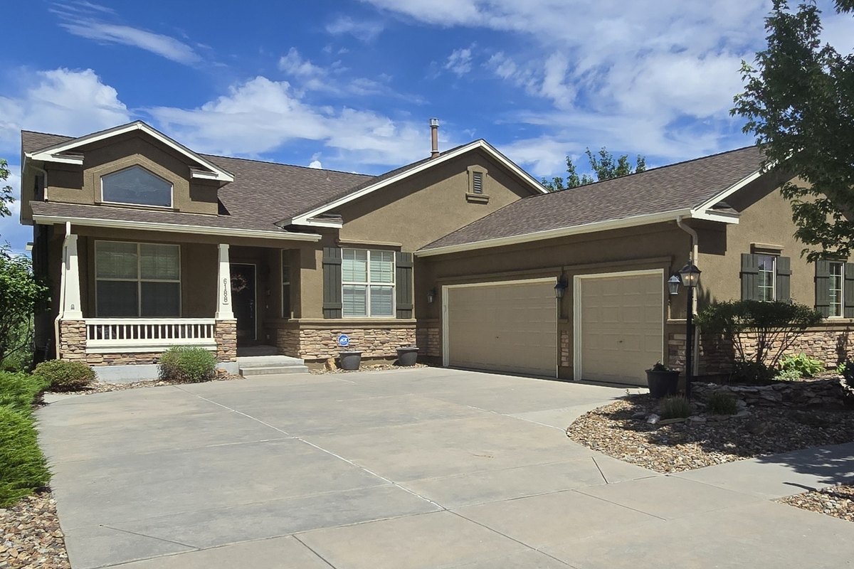 Finished brown stucco home with a covered front porch, stone accents, and a two-car garage