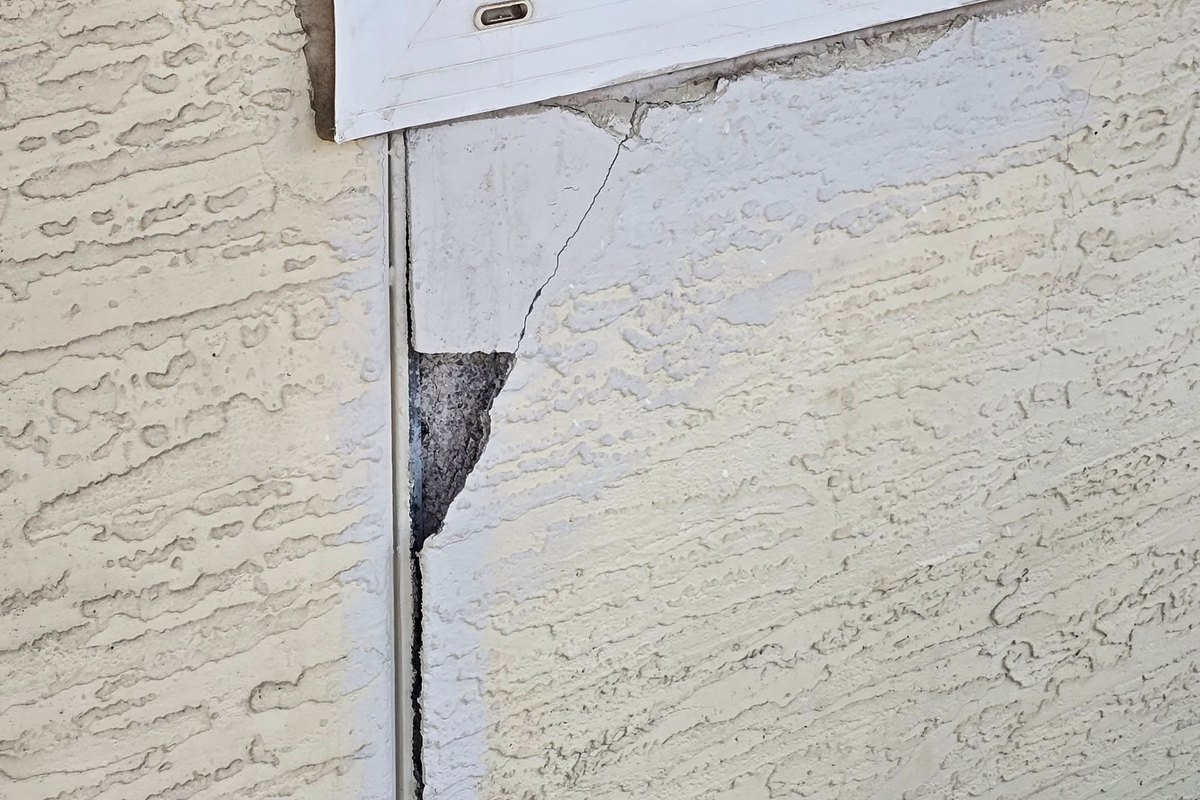 Stucco broken away at the corner below a window, with a crack running down the wall