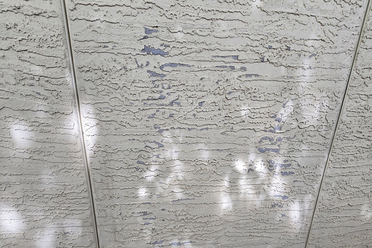 Textured stucco wall with its finish flaking away above the foundation