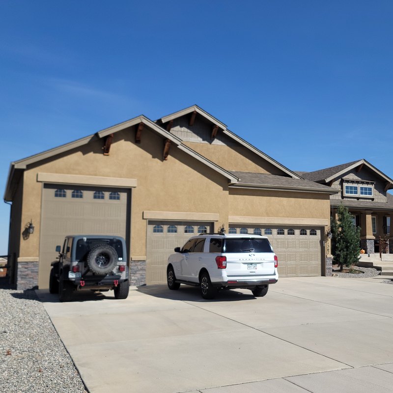 Tan stucco home with a three-car garage and a broad concrete driveway under a clear sky
